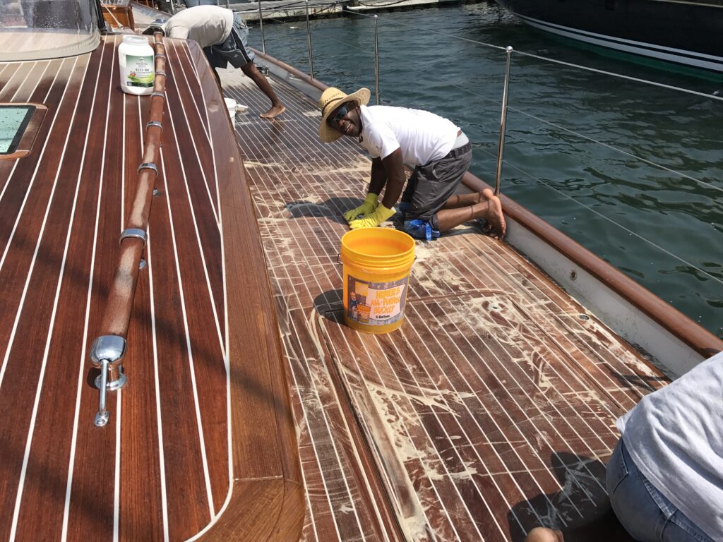 Deck being scrubbed across the grain with ECO Teak cleaner. Caulking is white.