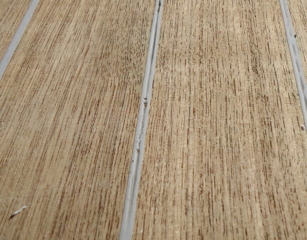 Close-up image of teak deck with gray caulking that has seam underfilled and with contaminates